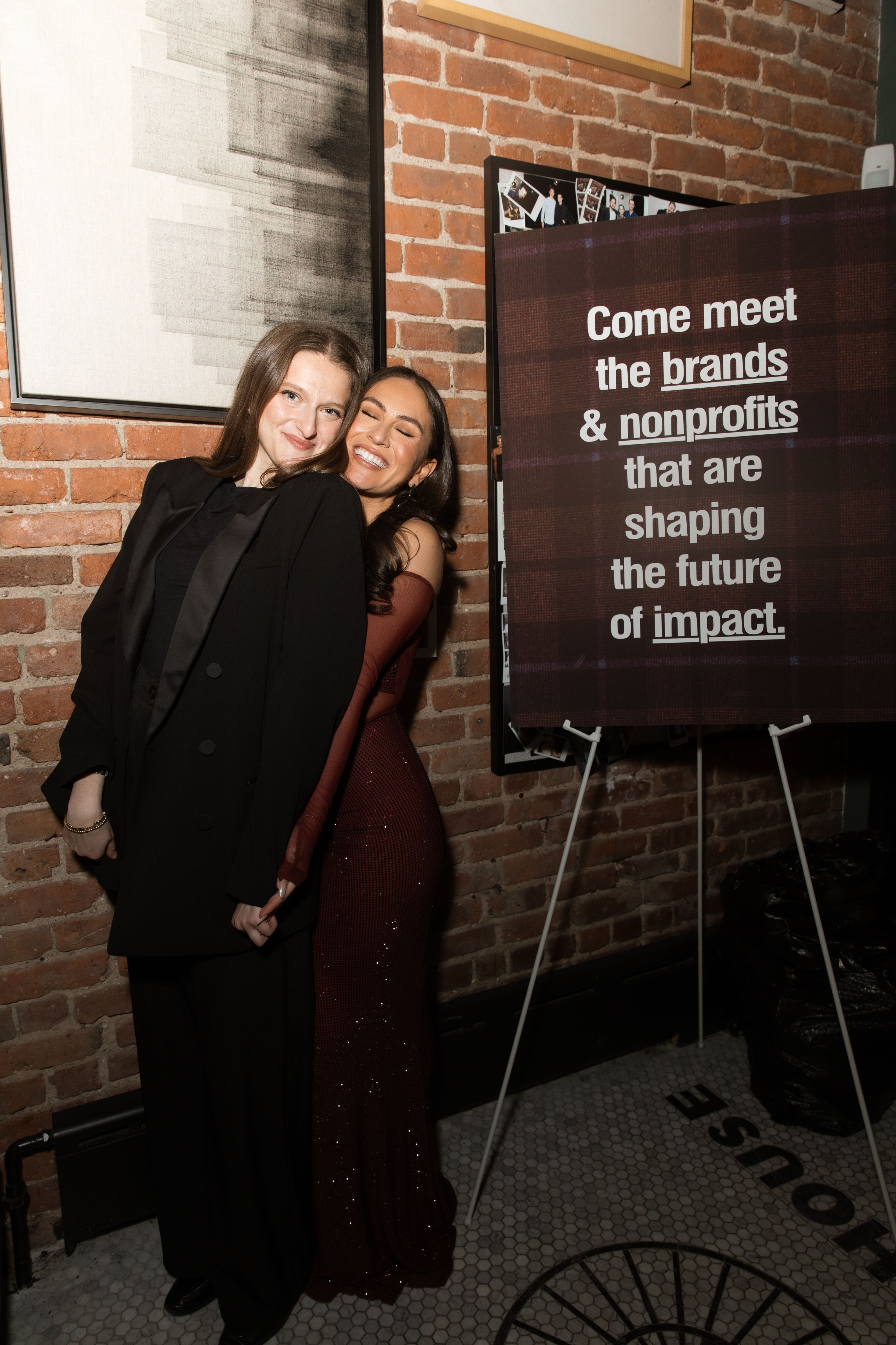 Two guests at ISR’s Social Impact House anniversary event pose beside signage highlighting brands and nonprofits shaping social impact.