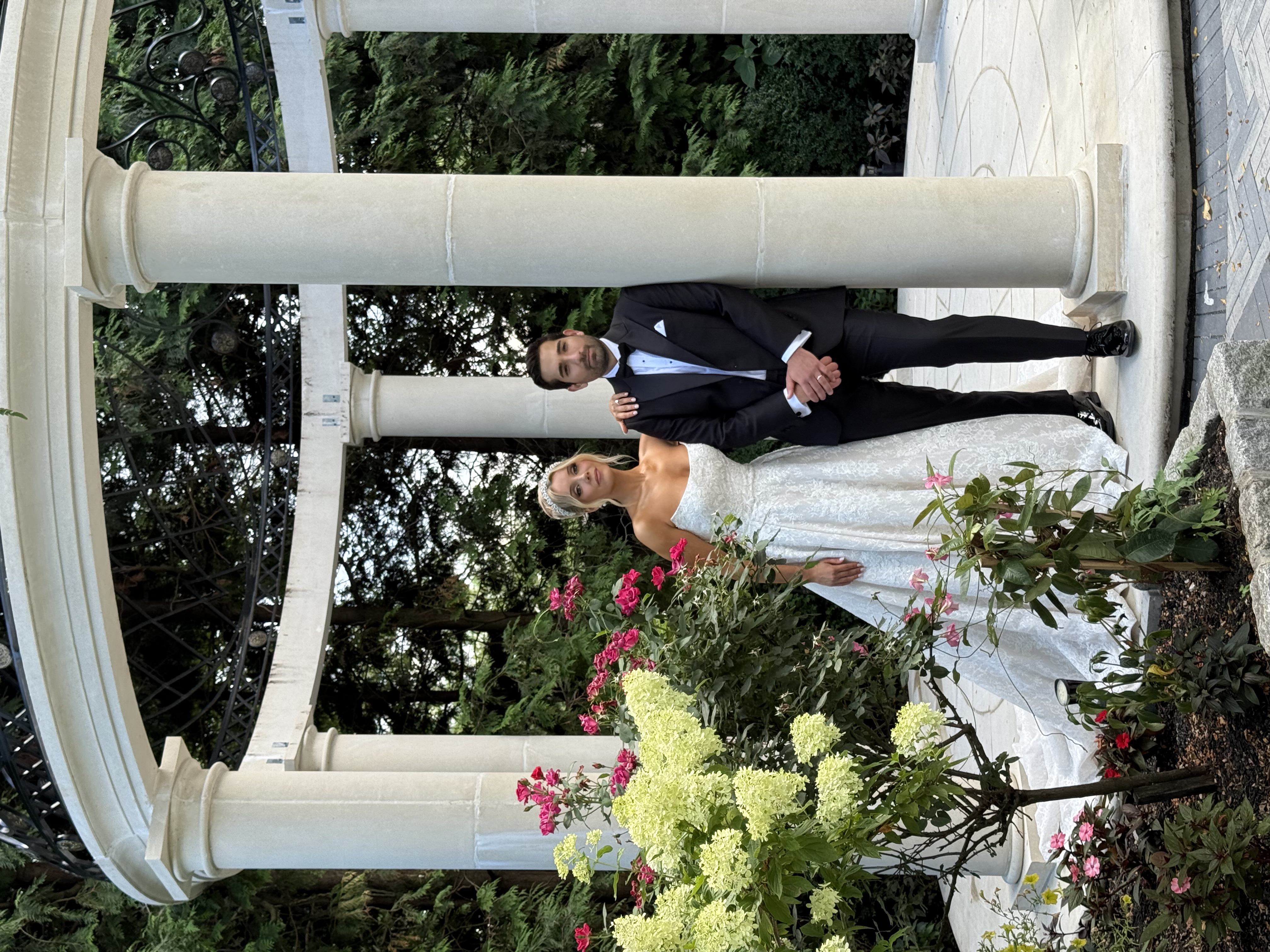 Bride and groom posing beneath a white stone gazebo surrounded by lush gardens at Florentine Gardens wedding venue in River Vale, New Jersey.