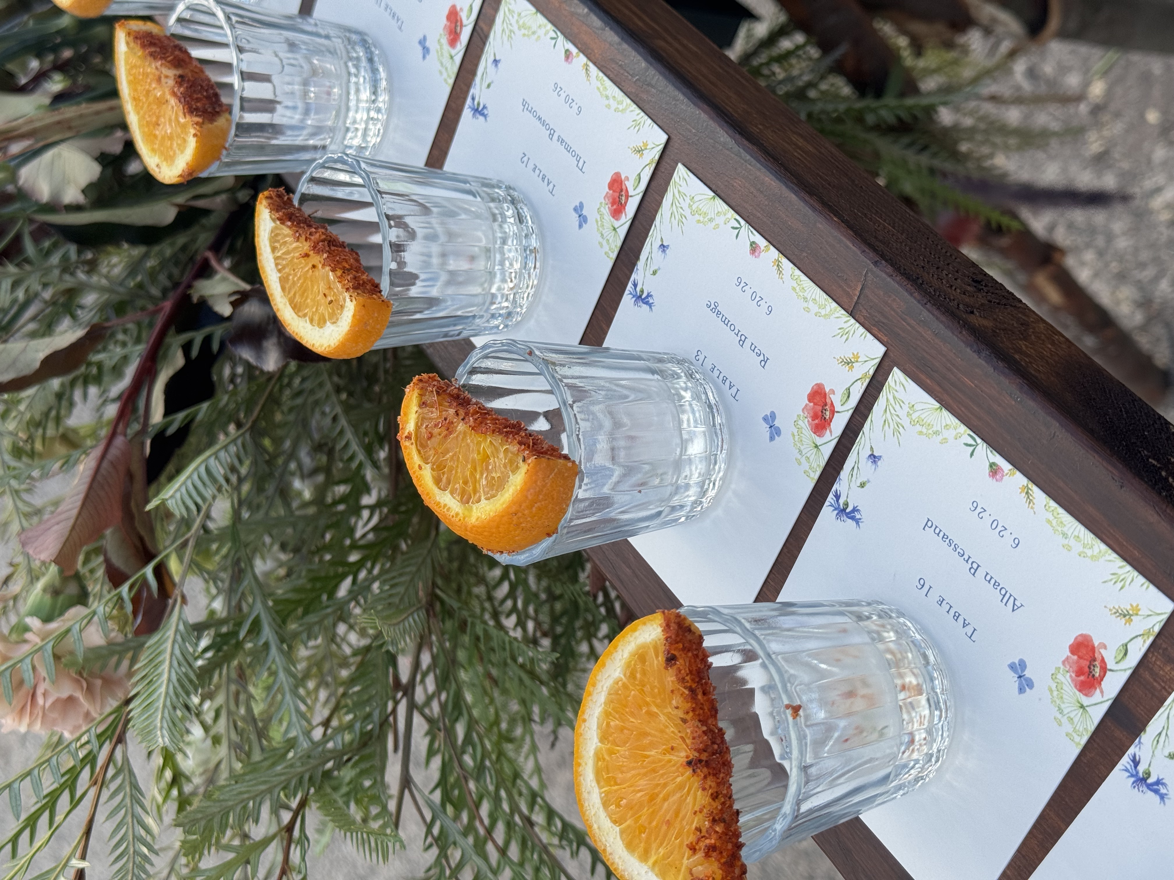 Escort cards displayed with glasses garnished with orange slices at an outdoor wedding reception