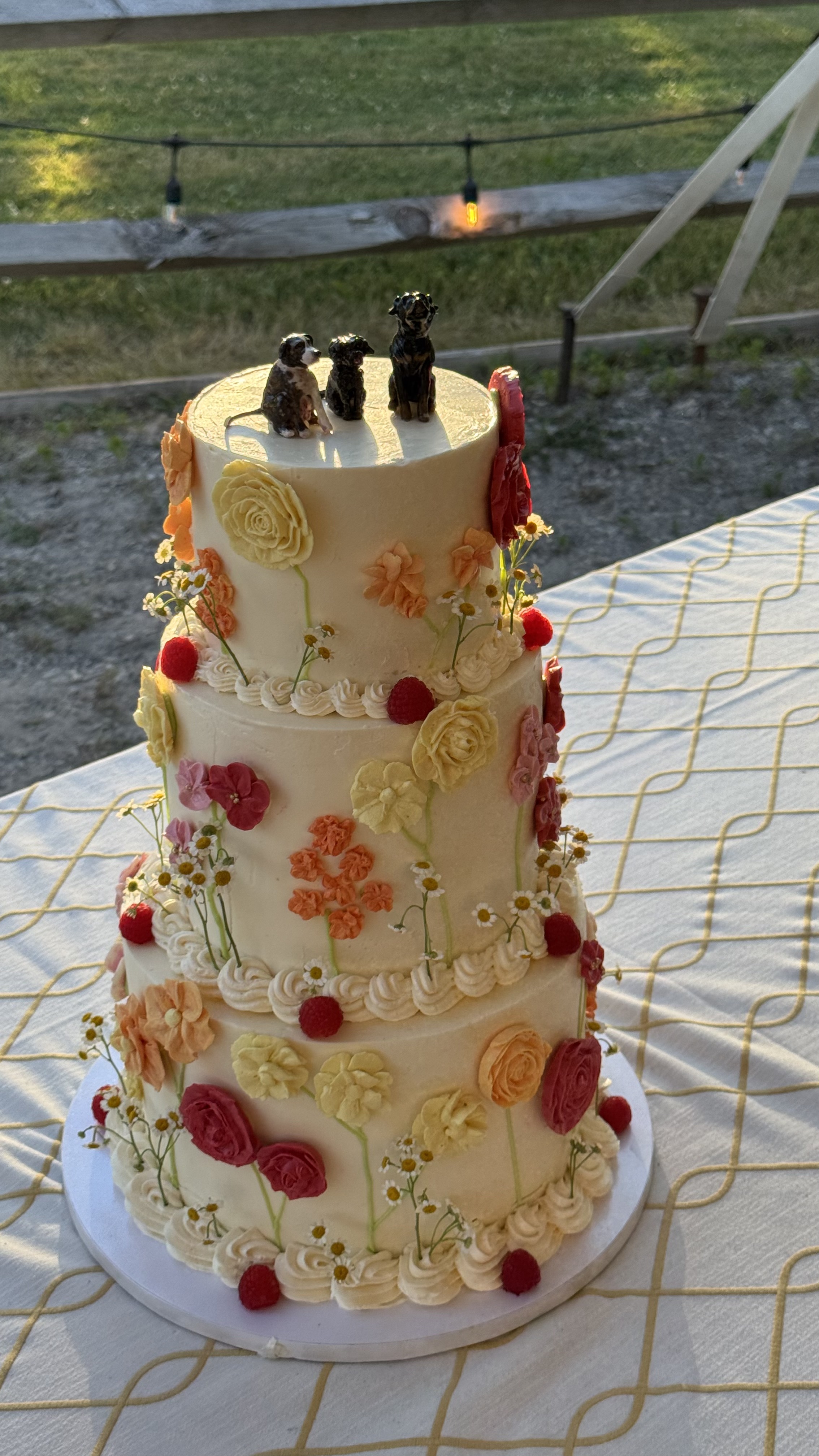 Three-tier wedding cake decorated with buttercream flowers and miniature dog figurines