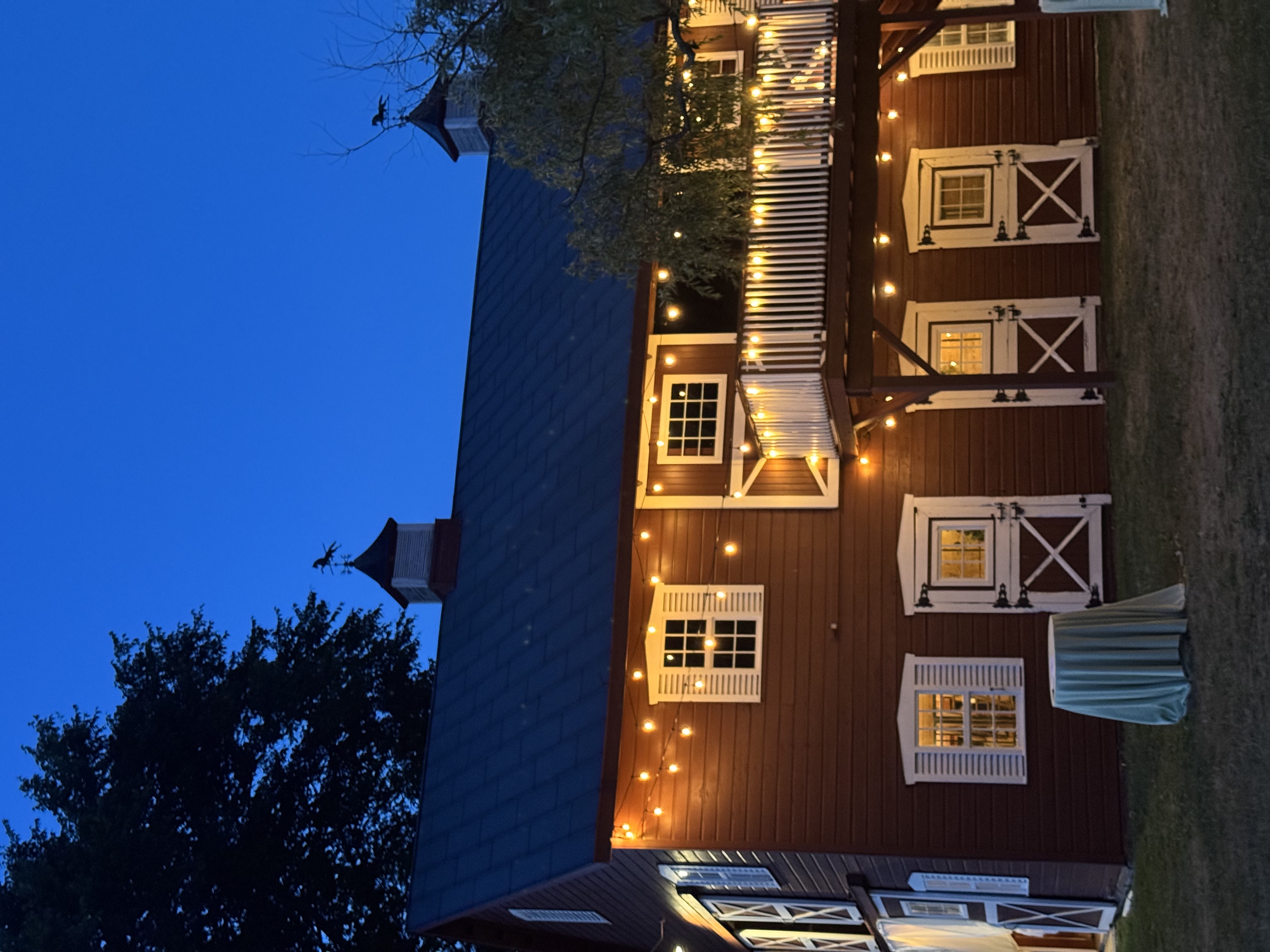 Rustic red barn illuminated with string lights at an outdoor wedding venue at dusk