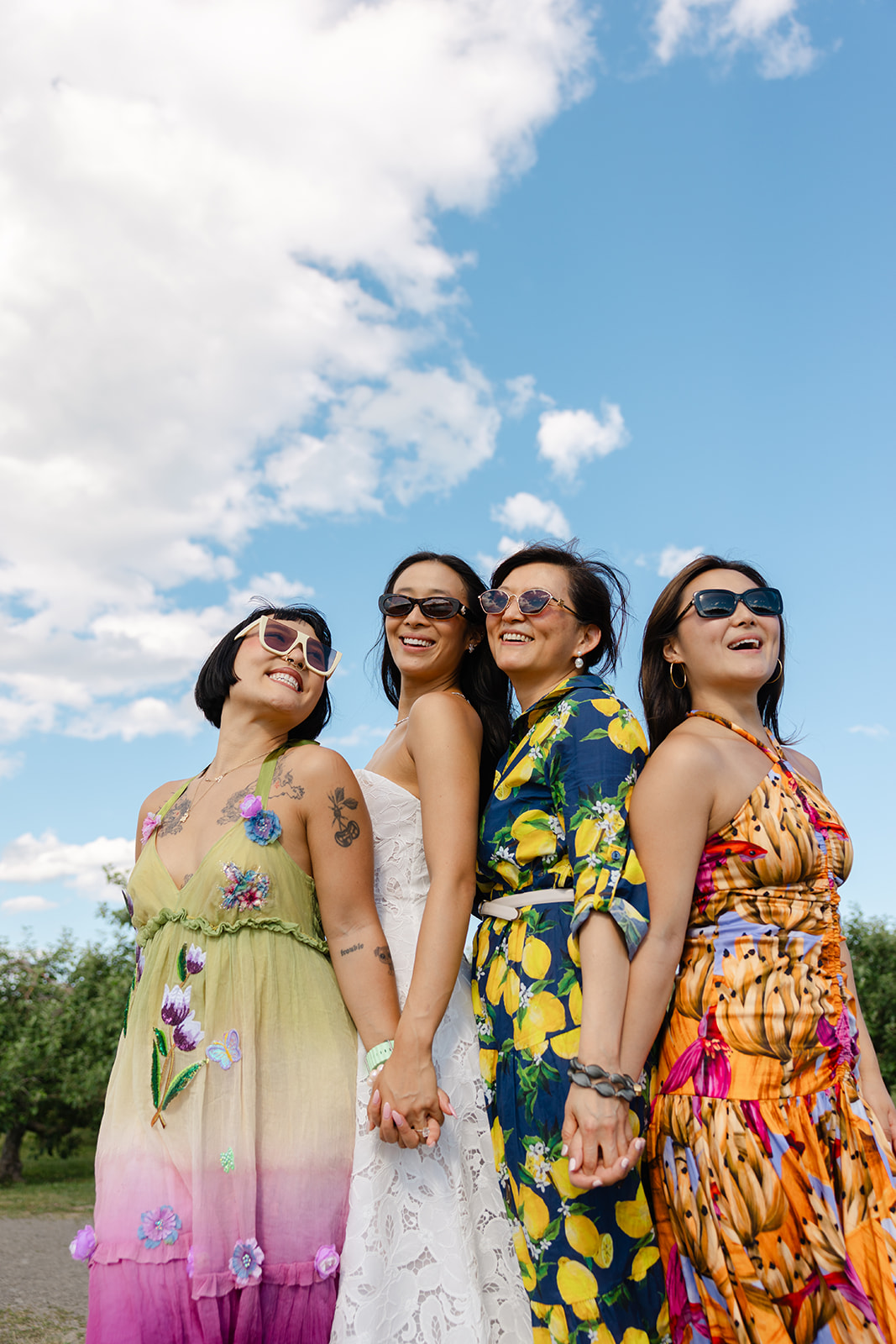 Bride poses hand in hand with family members during a wedding weekend celebration at La Luna Farm in New Paltz, New York, beneath a bright blue sky with scattered clouds.