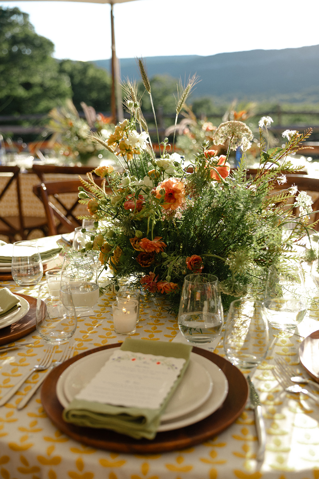 Elegant outdoor wedding reception table at La Luna Farm in New Paltz, New York, featuring lush seasonal floral centerpieces, candlelight, patterned linens, and mountain views in the background.