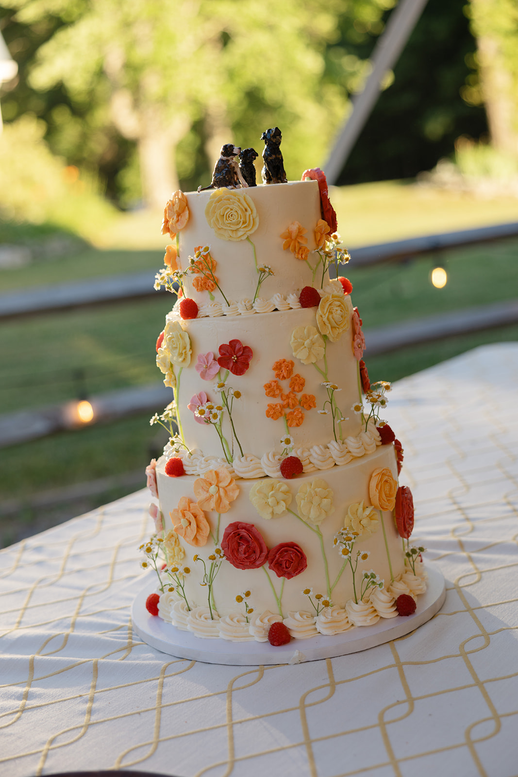 Three-tier wedding cake decorated with handcrafted buttercream flowers, fresh berries, and delicate wildflowers, displayed on a reception table at La Luna Farm in New Paltz, New York.